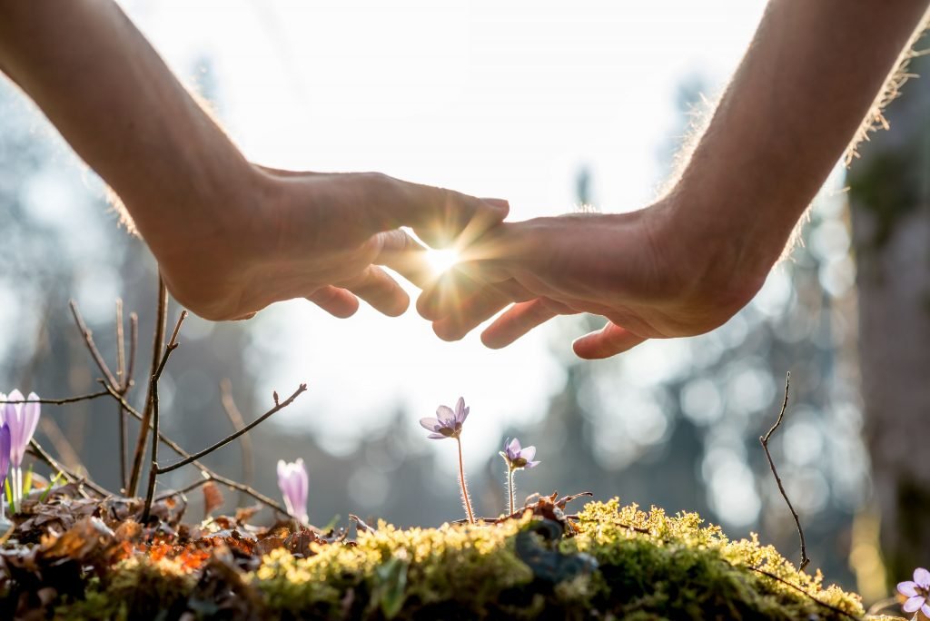 Two hands graze each other at sunrise depicting a new beginning and how alcoholism therapy can set you on a new life course after alcohol rehab.
